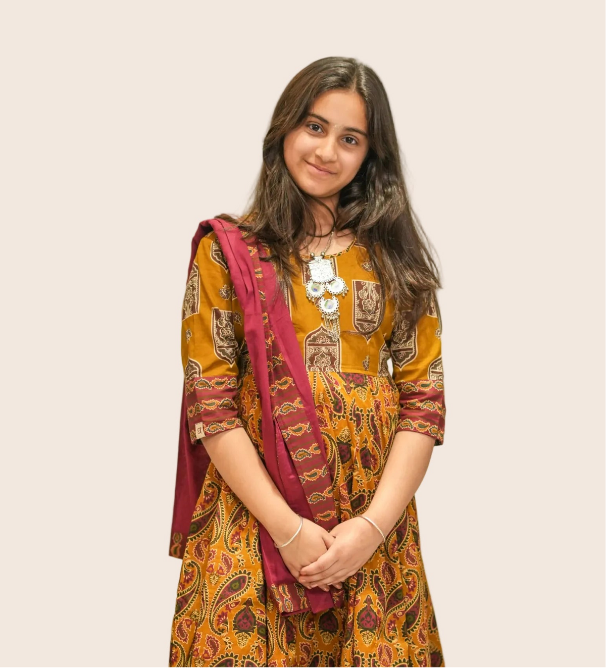 Girl wearing a traditional outfit with a yellow and red patterned dress in an indoor setting.